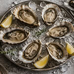 Opened oysters on crushed ice with lemon wedges, beside a glass of white wine, a small bowl of mignonette and an oyster knife