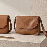 Two tan crossbody bags side by side on a stone plinth, one smooth and new, the other creased and scuffed at the edges