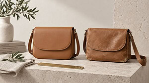 Two tan crossbody bags side by side on a stone plinth, one smooth and new, the other creased and scuffed at the edges